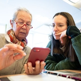 Smartphone-Sprechstunde für Senioren: Eine junge Frau erklärt einer älteren Funktionen am Handy. Seit Jahrzehnten labeln Gesellschaften Alterskohorten in bestimmte "Generationen", die vermeintlich Erfahrungen und Verhalten miteinander teilen. Doch was ist dran an Zuschreibungen wie Boomer, Millenials oder Gen Z?