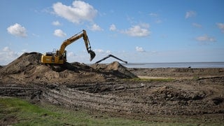 Auf einer Baustelle zur Deichverstärkung am Hauke-Haien-Koog nahe des Fähranlegers Schlüttsiel wird im Juli 2023 mit schwerem Gerät die Deichkrone des alten Deiches erhöht. Die Klimadeiche in Schleswig-Holstein sind an steigende Meeresspiegel und höhere Sturmfluten angepasst.